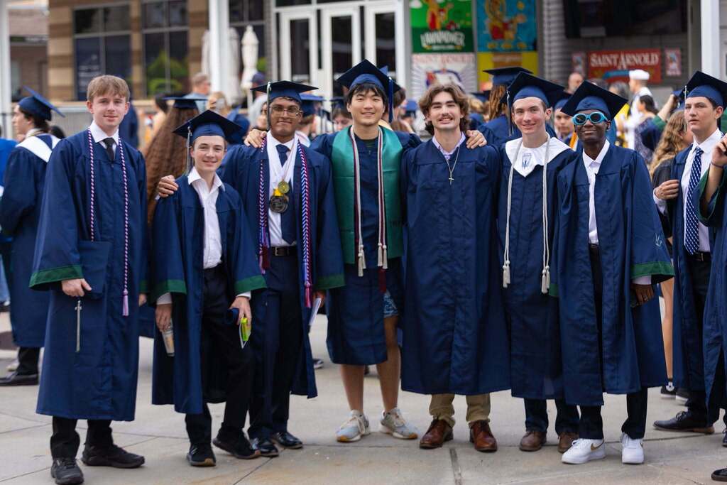 Seven male students in dark blue robes at graduation.