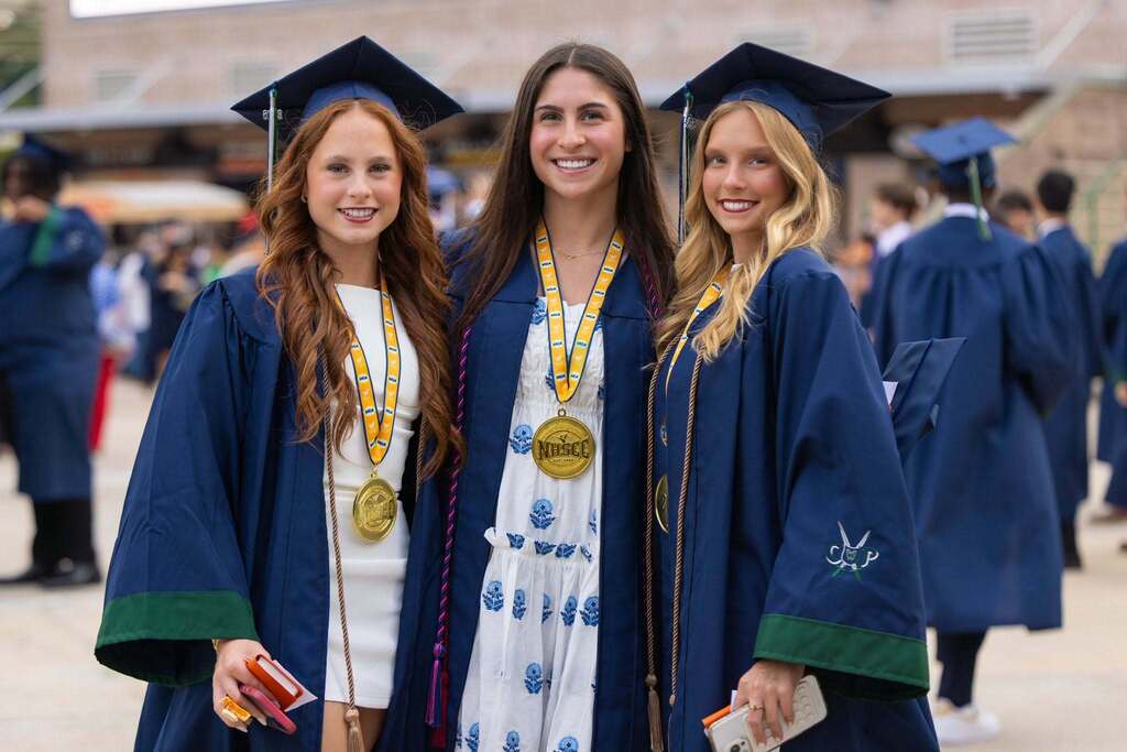 Three female students in dark blue caps and gowns.
