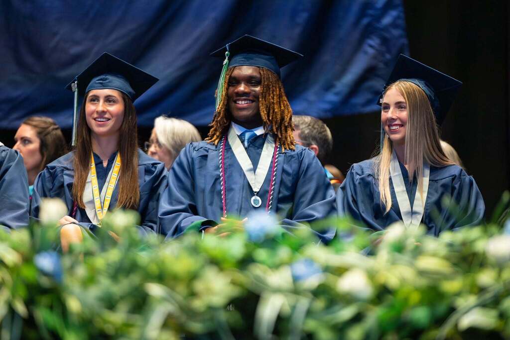 Three graduates smile on stage.