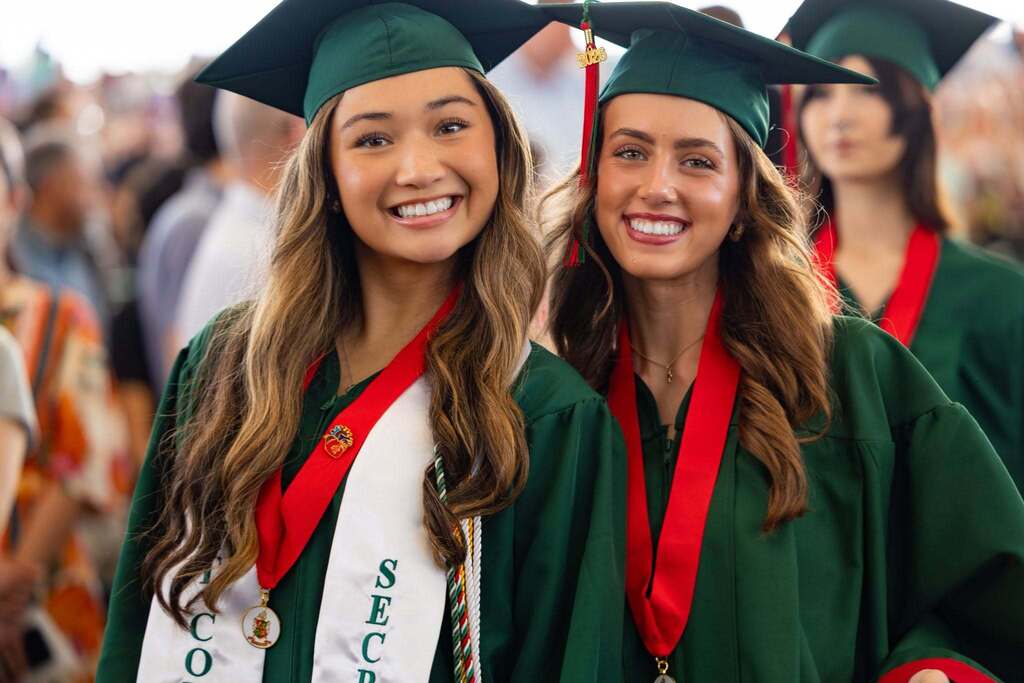 Two female graduates in green caps and gowns.