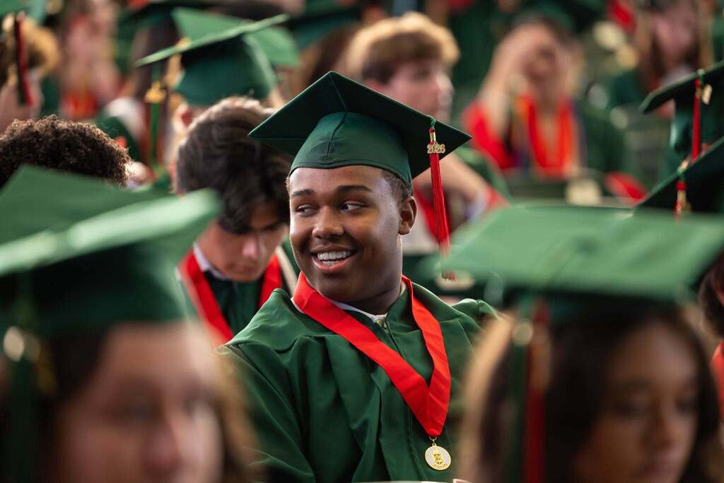 Male graduate in green cap and gown smiles and looks back.