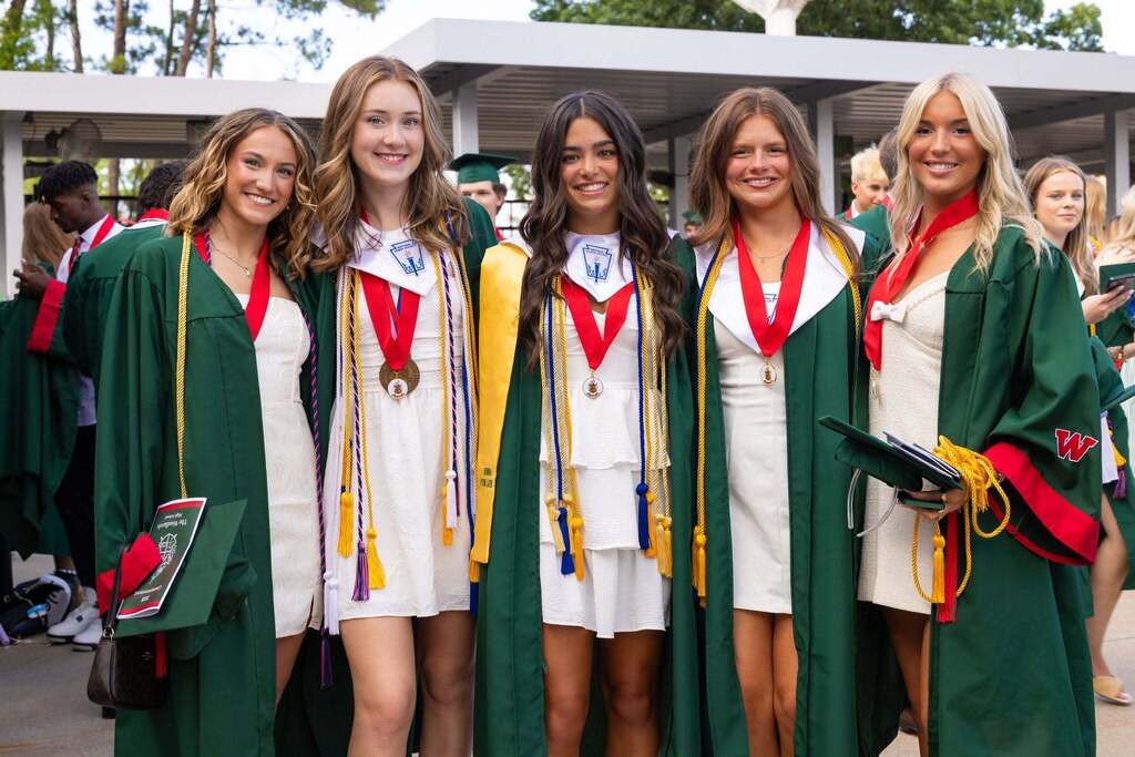Five female graduates in white dresses and green caps and gowns.