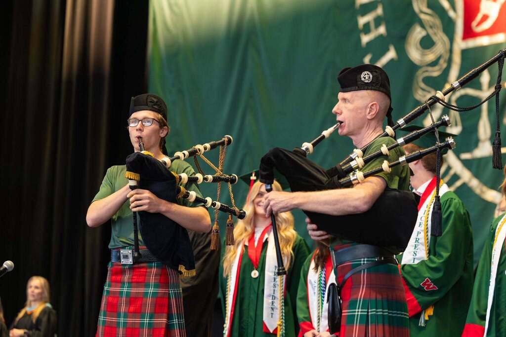 Two men play bagpipes during graduation ceremony.