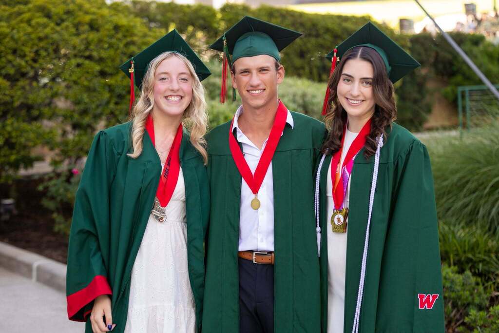 Two female and one male student in green graduation caps and gowns.