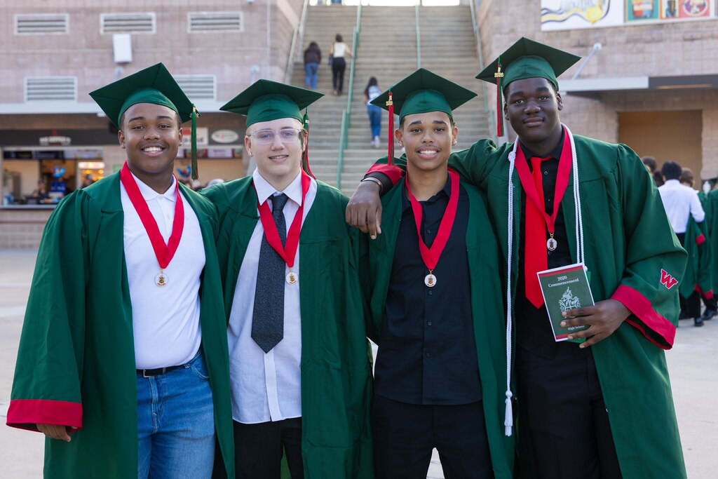 Four male graduates in green caps and gowns.