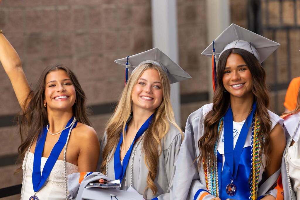 Three female graduates in gray caps and gowns.