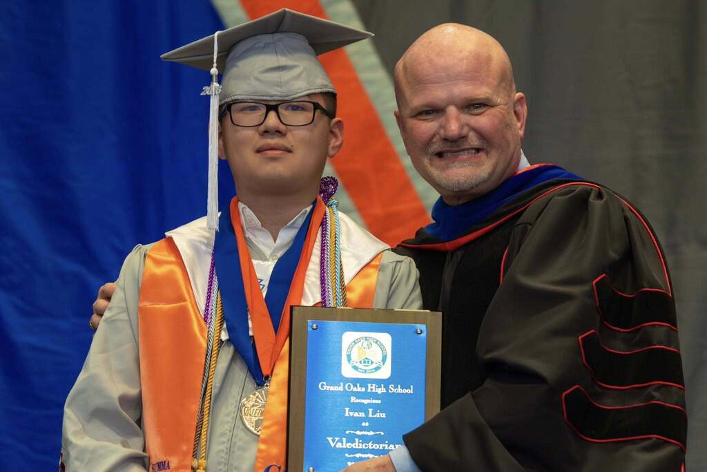 Valedictorian and Superintendent hold award plaque.