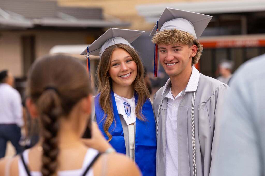 Male and female student in gray caps and gowns take a photo.