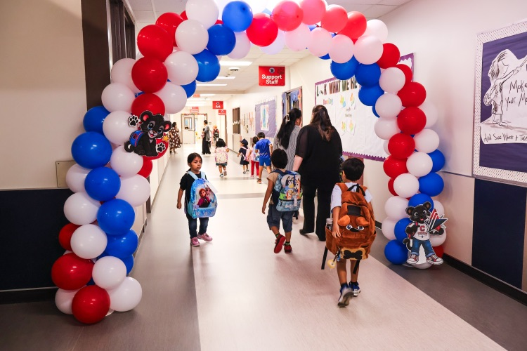 Students walking through a red, white, and blue balloon arch.