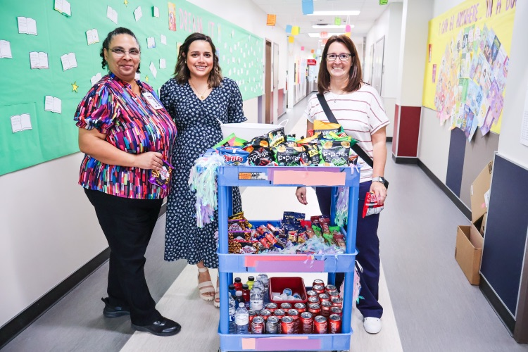 Three staff members standing beside a snack and drink cart.