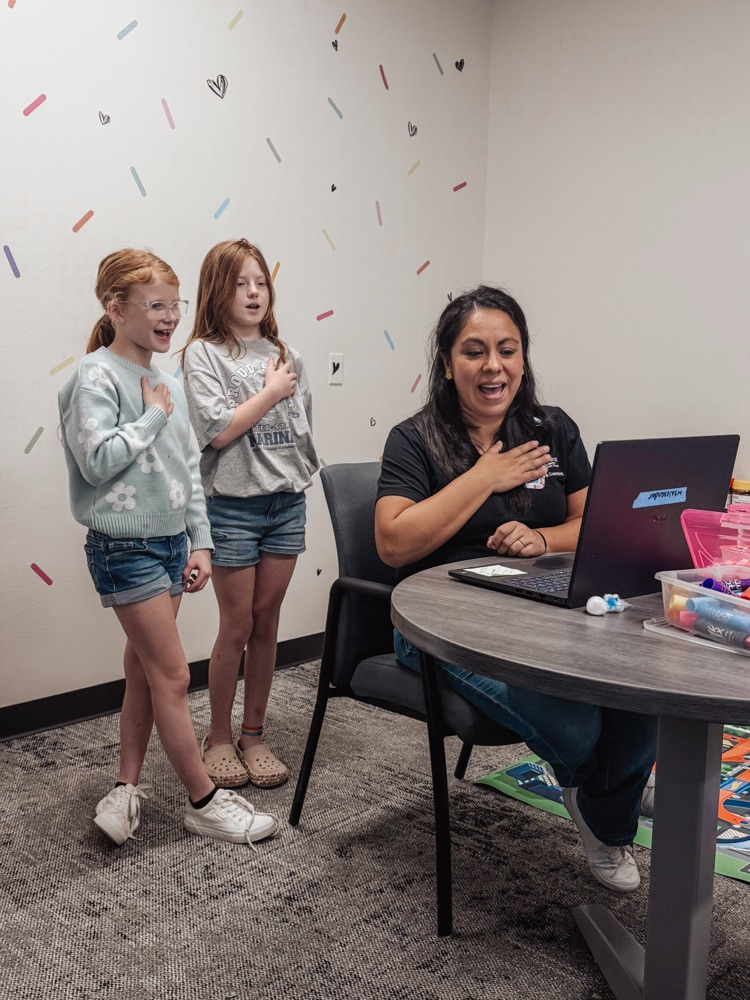 Two students and a staff member recording morning announcements with their hands over their hearts.