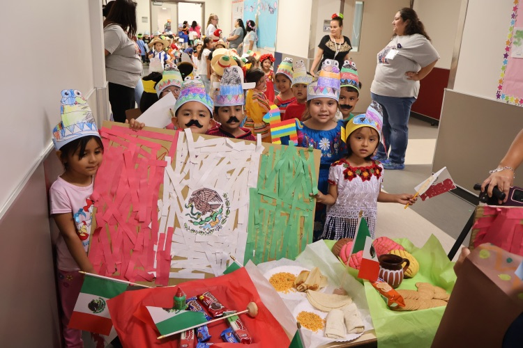 Students celebrate Mexican heritage with colorful traditional attire, handmade decorations, and Mexican flags during a school parade.
