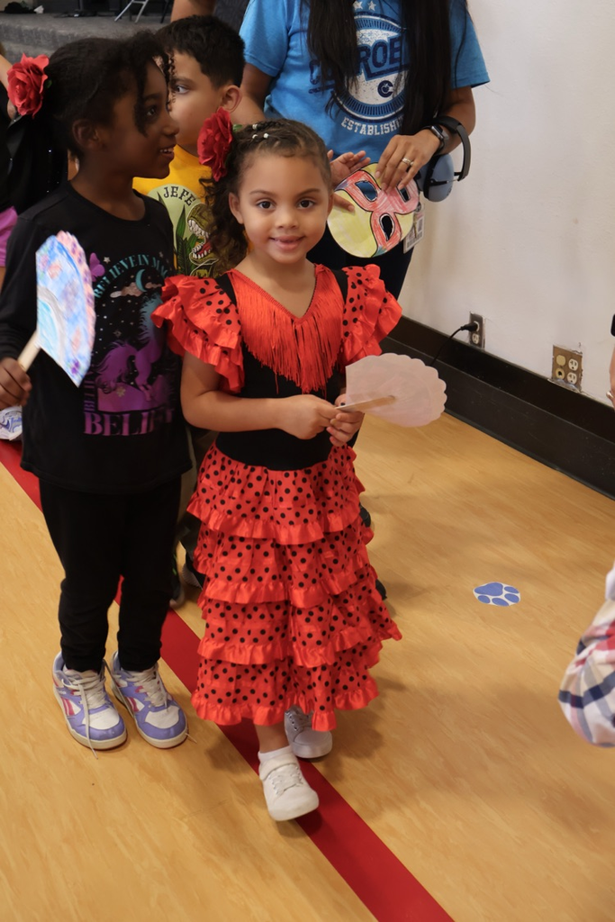 Students celebrate Hispanic heritage in colorful outfits, including a traditional red flamenco-style dress, while holding handmade decorations.