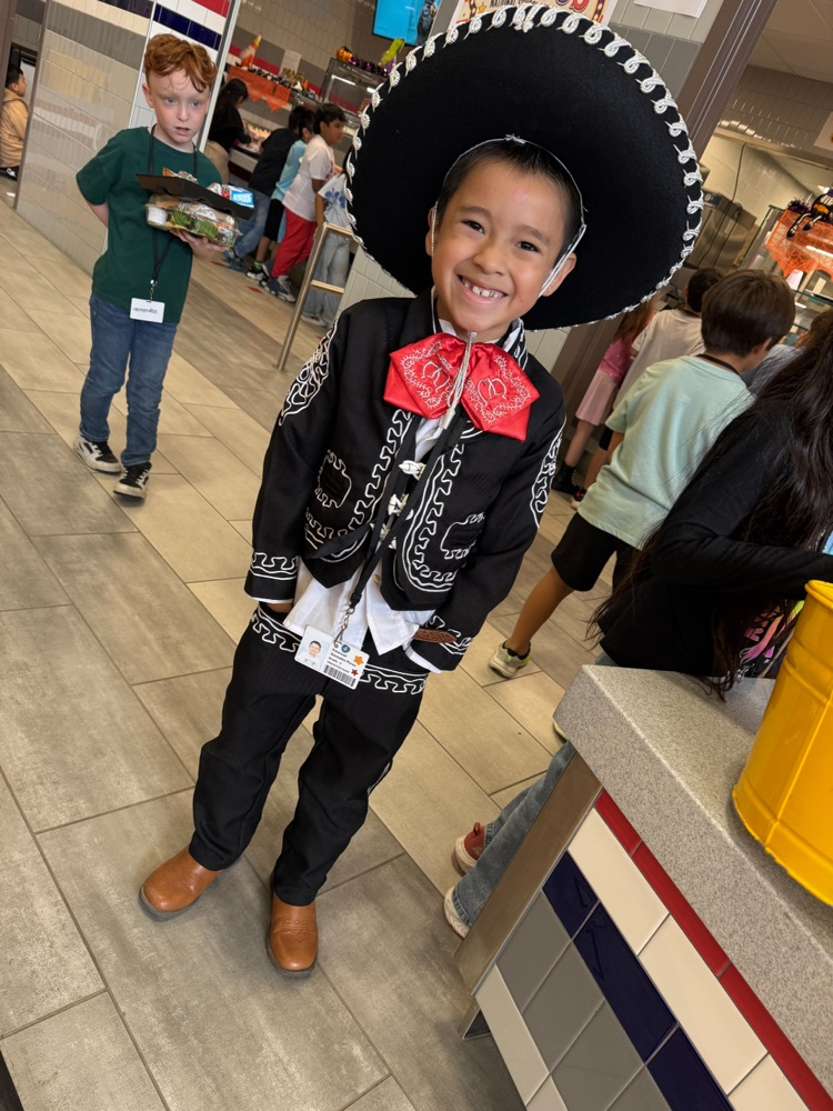 A smiling student celebrates Hispanic heritage wearing a traditional black charro suit, red bow tie, and sombrero.