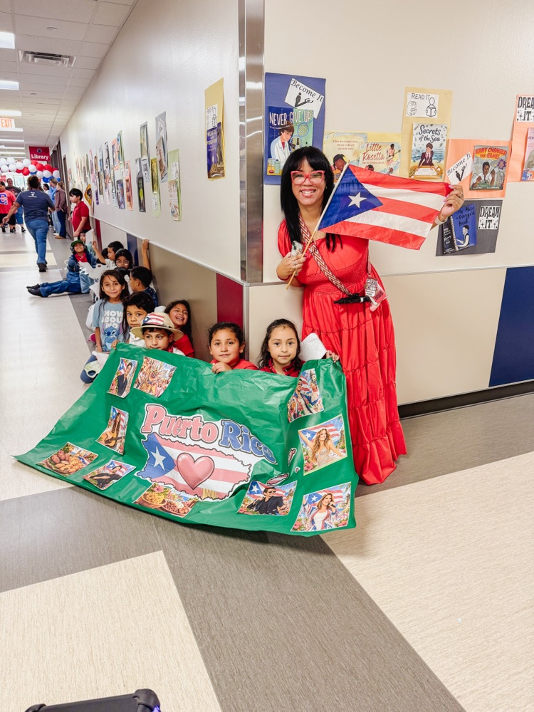 A teacher and students proudly celebrate Puerto Rican heritage with a Puerto Rican flag and colorful cultural banner.