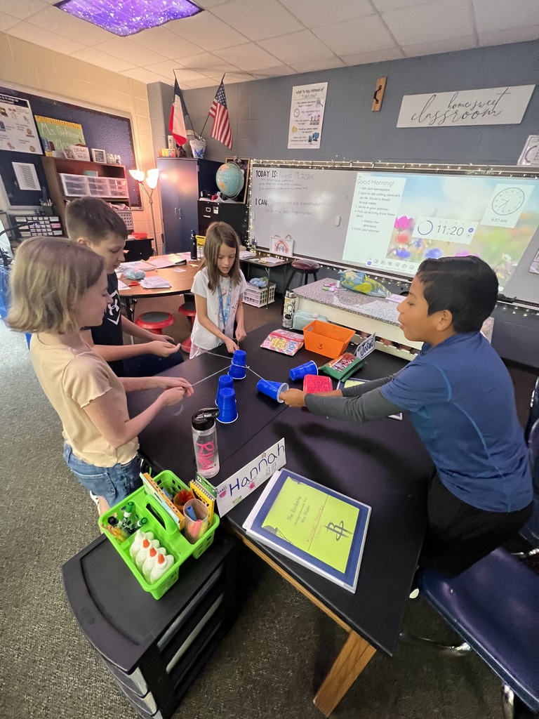 Four students working together on a science experiment with plastic cups and string
