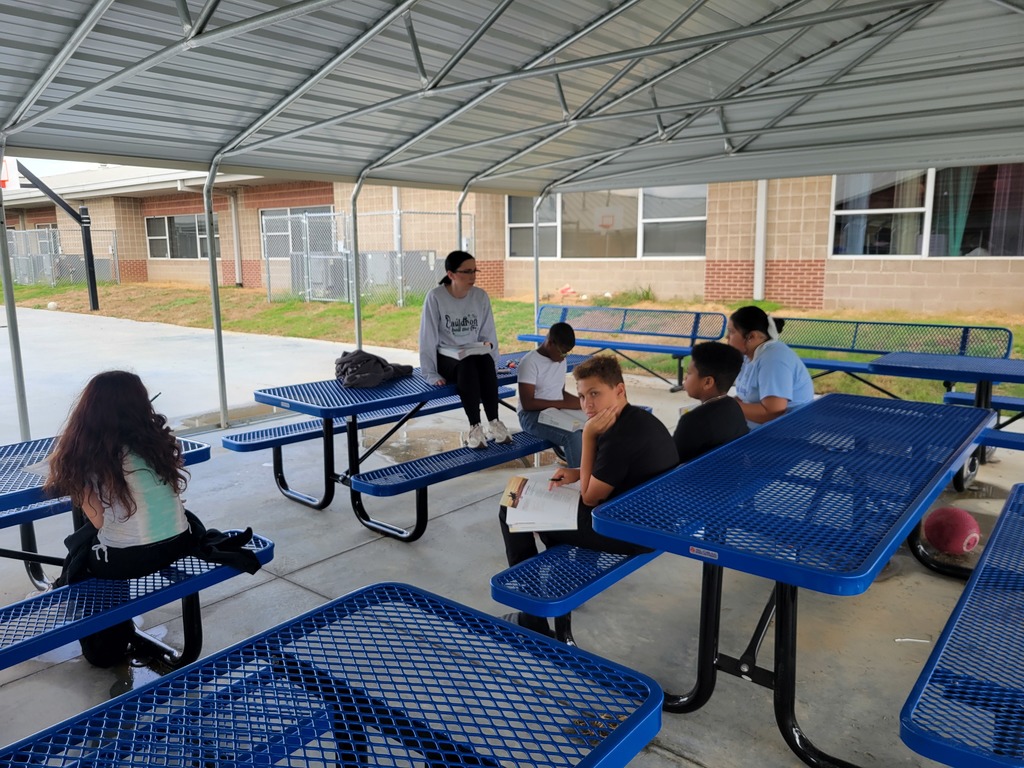 Students in outdoor classroom sitting on blue benches reading and annotating poetry