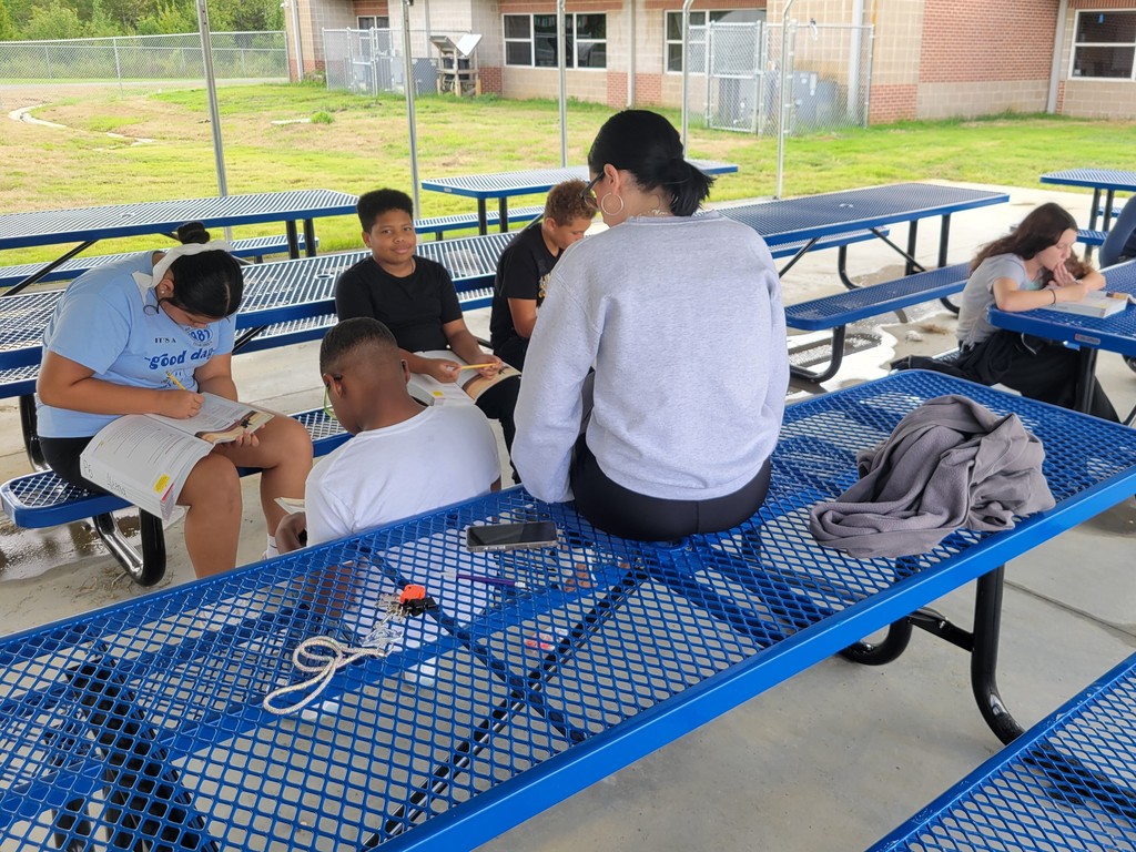 Students in outdoor classroom sitting on blue benches reading and annotating poetry