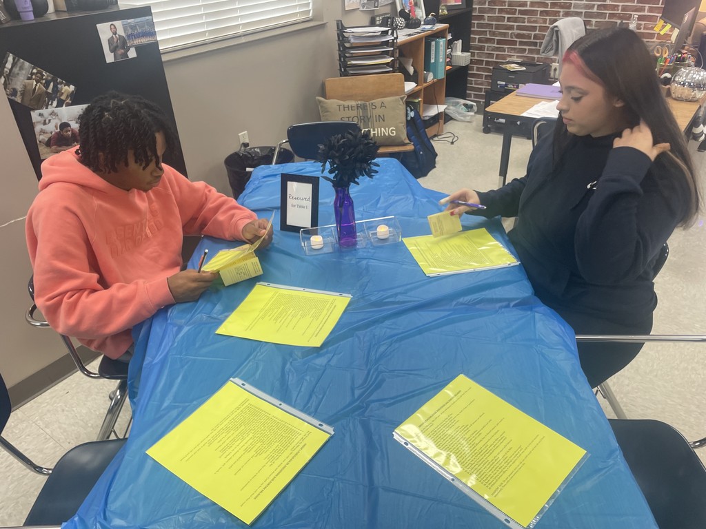 Students sitting or standing around a table discussing various topics.