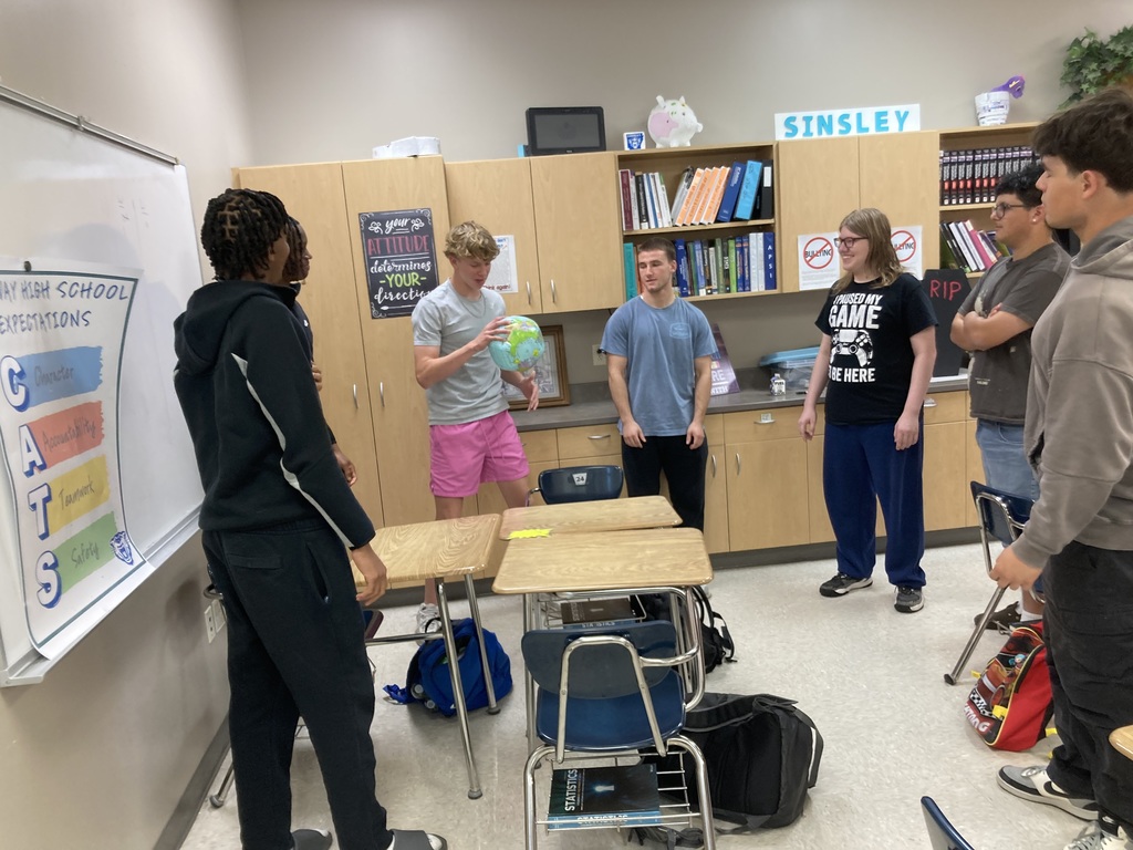 students watch on as another catches an inflatable globe and looks to see whether or not his fingers landed on water or land.