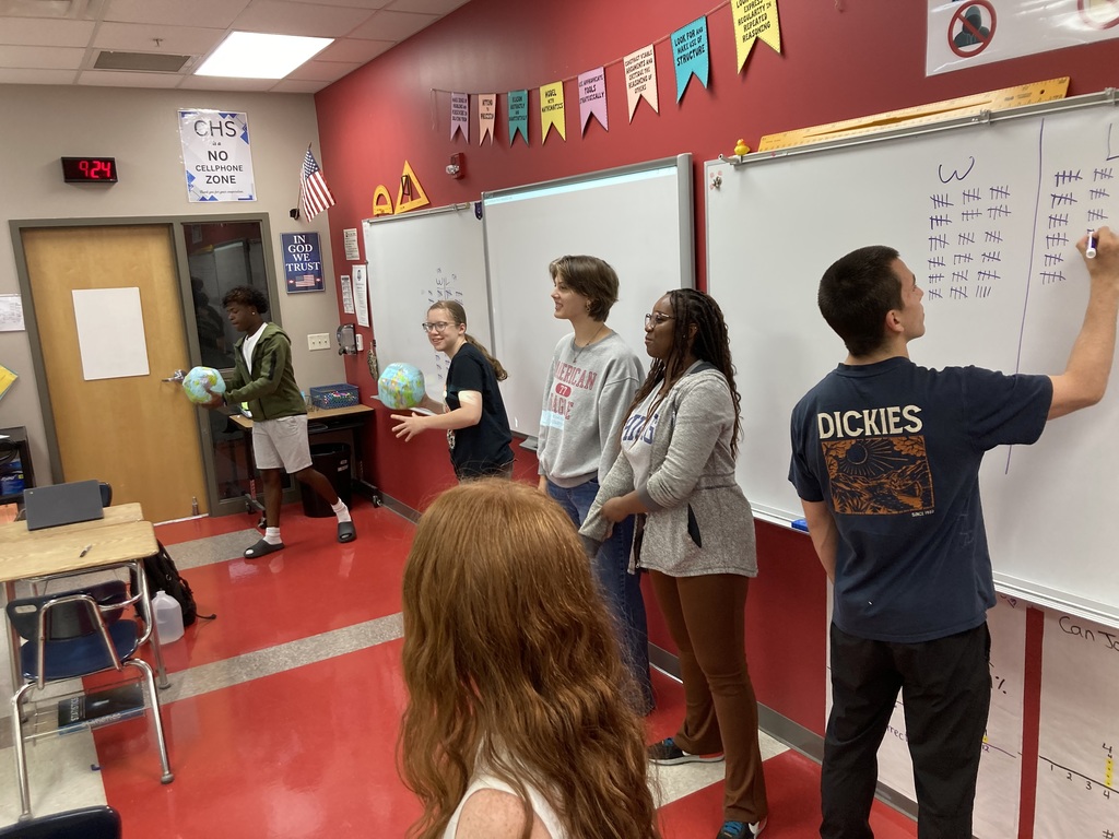 Students toss an inflatable globe to a partner. Another student records the results.