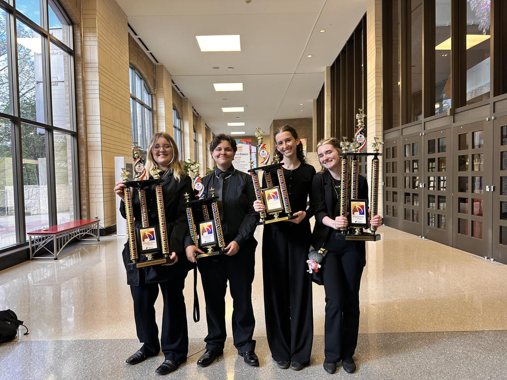 Orchestra students posing with trophies awarded for performance.
