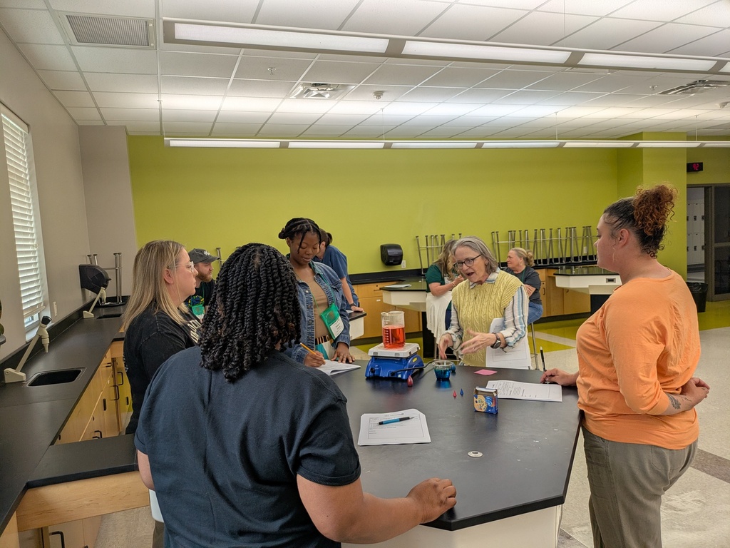 A small group of teachers around the lab table being guided by a presenter.