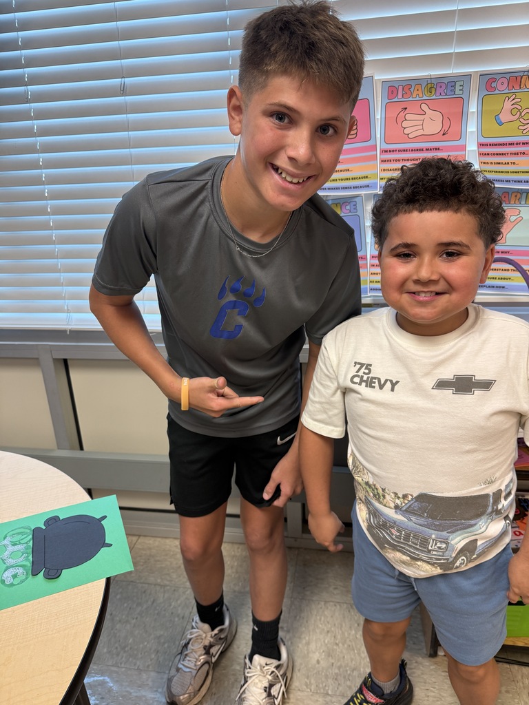 Two students smiling at the camera with one of the students bubbly witch's cauldron art creation