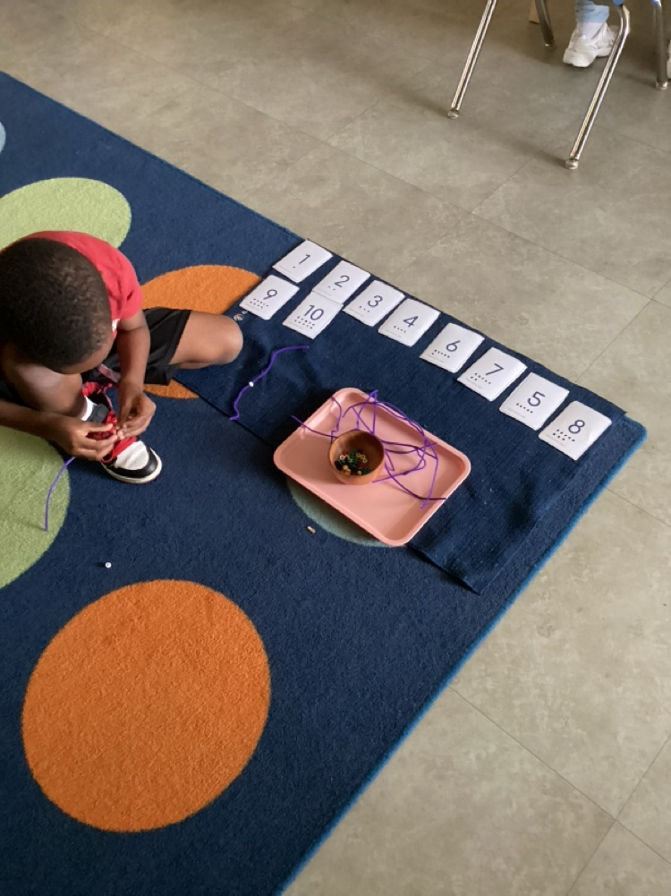 child who has the numbers laid out so neatly on his work mat while he works on stringing the number of beads for each number card beads