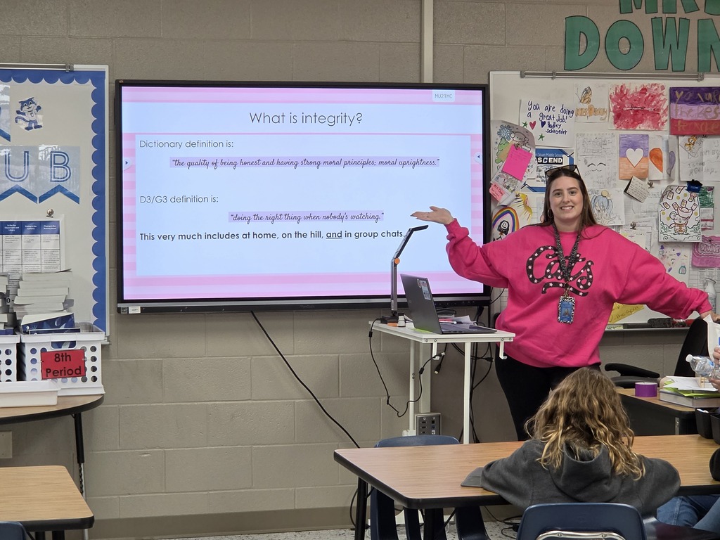 Mrs. Downey smiling while pointing at her white board
