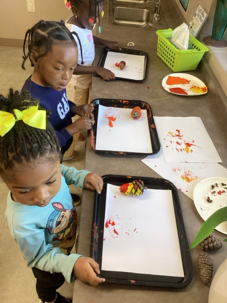 children using trays and pine cones dipped in fall colors, rolling the pine cone back and forth to make patterns