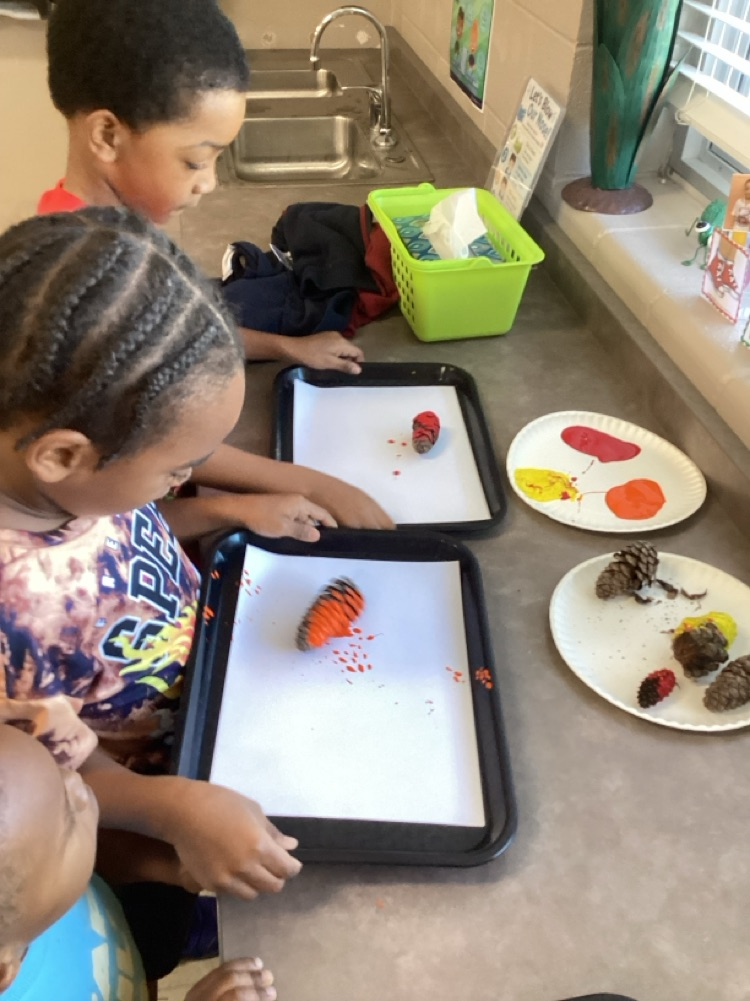 child rolling a pine cone on a tray back and forth with a painted pine cone