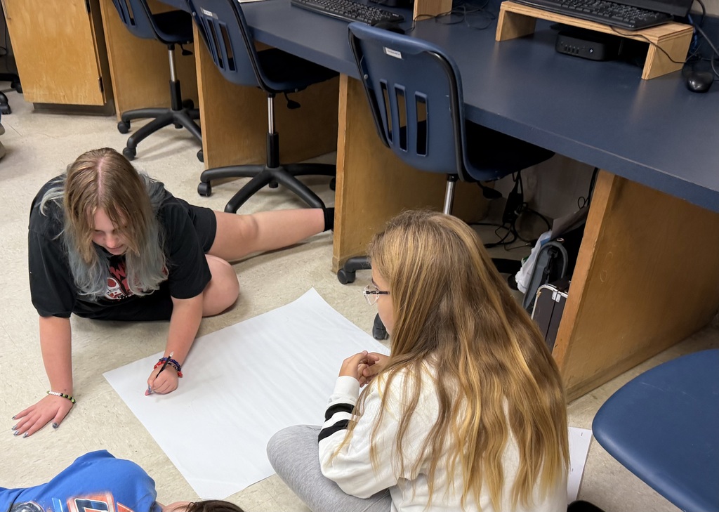 Students sitting in the floor drawing on large sheets of paper, creating their micro mansions
