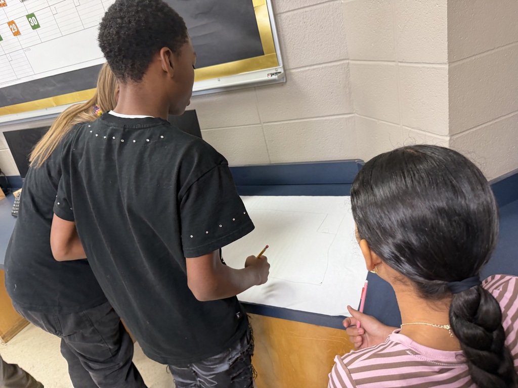 Students standing at a desk drawing on large sheets of paper, creating their micro mansions