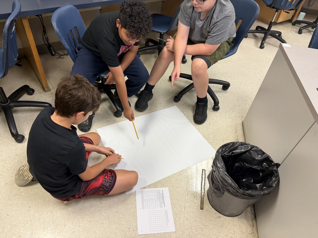 Students sitting in the floor drawing on large sheets of paper, creating their micro mansions