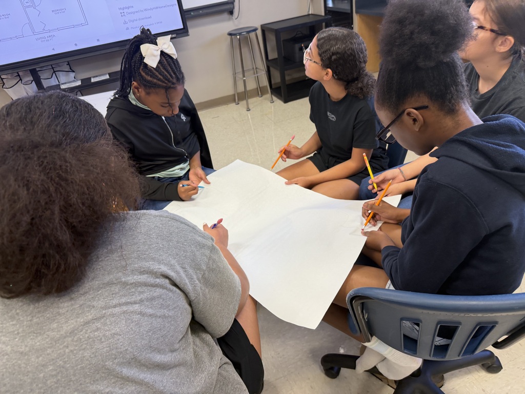 Students sitting in the floor drawing on large sheets of paper, creating their micro mansions