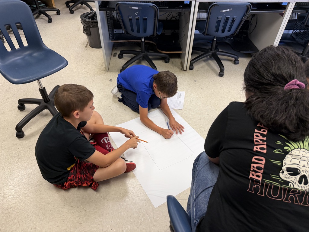 Students sitting in the floor drawing on large sheets of paper, creating their micro mansions