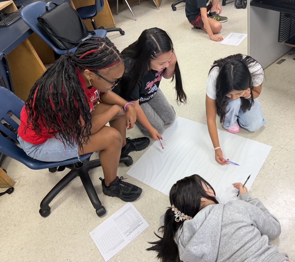 Students sitting in the floor drawing on large sheets of paper, creating their micro mansions