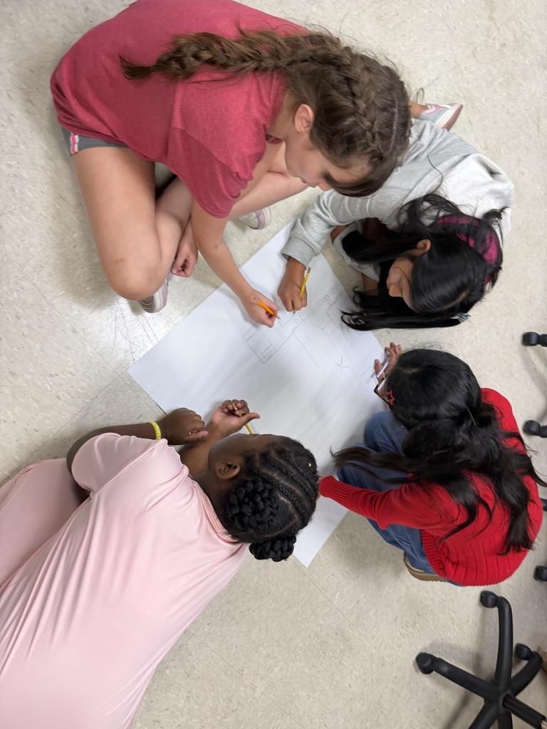 Students sitting in the floor drawing on large sheets of paper, creating their micro mansions