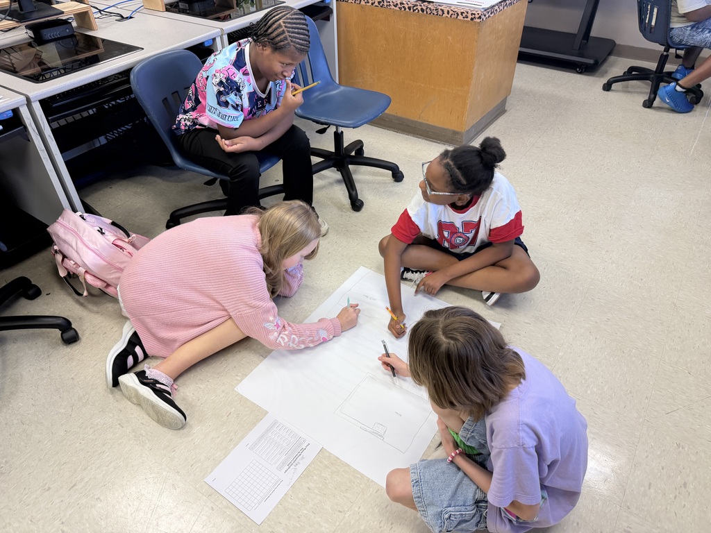 Students sitting in the floor drawing on large sheets of paper, creating their micro mansions