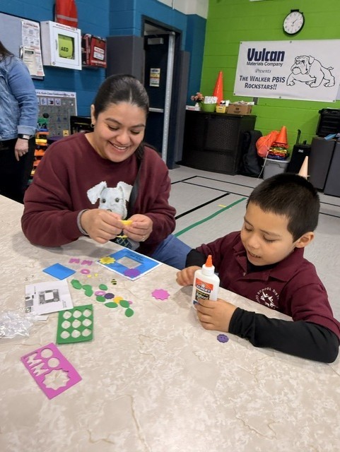 A woman and child enjoy a craft activity at a table, using colorful paper and glue. Both are smiling, creating a warm, joyful atmosphere.