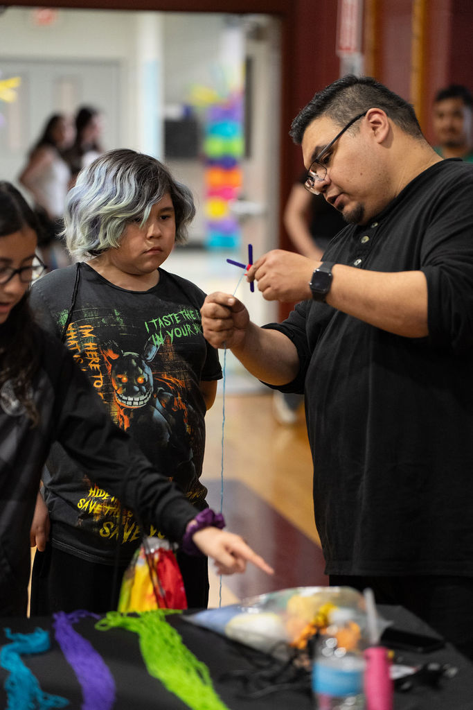 A person demonstrates how to make crafts with colorful threads to a child at an indoor event. The atmosphere is educational and engaging.