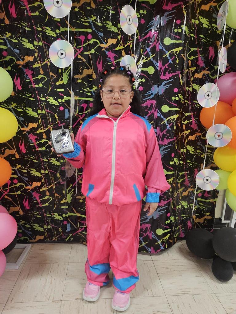 Girl in a bright pink tracksuit stands against a vibrant, colorful backdrop, holding a portable CD player. Balloons and CDs create a playful atmosphere.