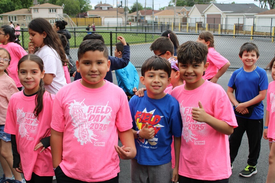 A group of children wearing pink and blue shirts, smiling and posing for the camera during a school field day event.