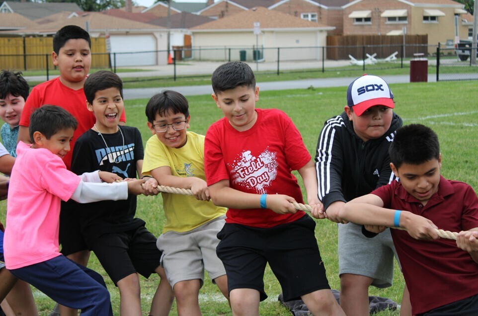 A group of children playing tug-of-war on a grassy field.