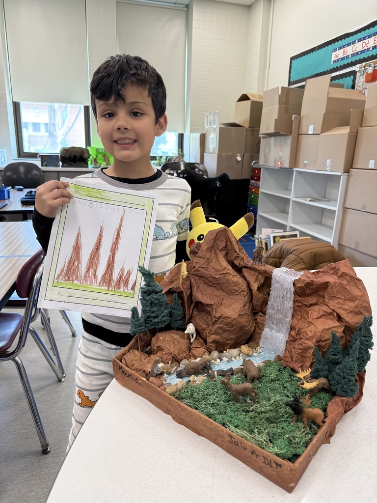 A boy proudly displays a paper model of a mountain, showcasing his creativity and craftsmanship.