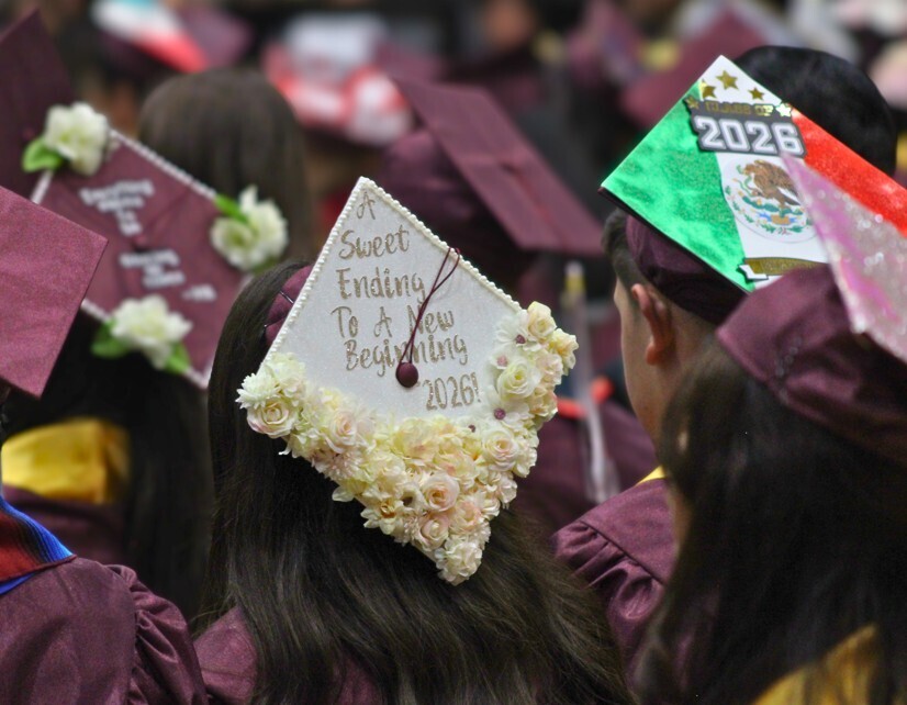 Close-up view of graduates in burgundy robes featuring decorated mortarboards, one with flowers and "A Sweet Ending To A New Beginning 2026," and another with the Mexican flag colors and "2026."