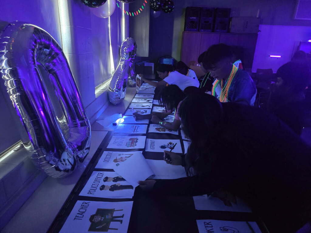 Children wearing neon necklaces participate in a glow-in-the-dark activity with large balloons and job-themed worksheets.