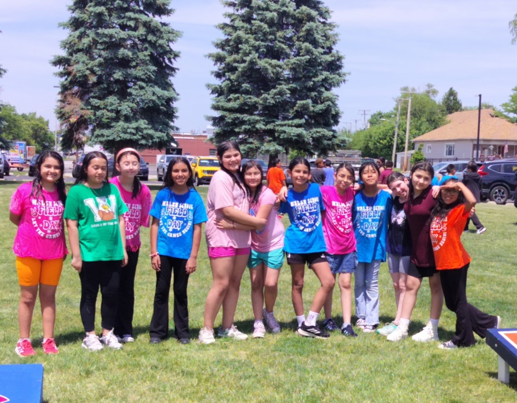 A group of diverse elementary school girls in colorful t-shirts pose for a photo outdoors during a field day event.