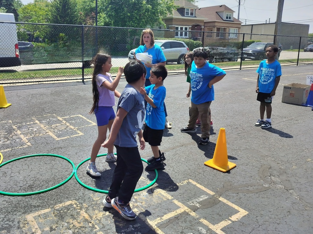 Children in blue t-shirts participate in an outdoor school activity with hula hoops and cones.